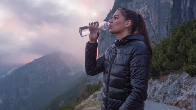 女人站在群山环绕的悬崖上喝水