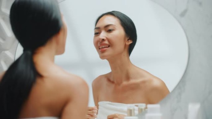 美丽的亚洲女人用牙线清洁她的天然洁白的牙齿，微笑在浴室的镜子。快乐的女性做她的美容早晨例行公事。牙齿