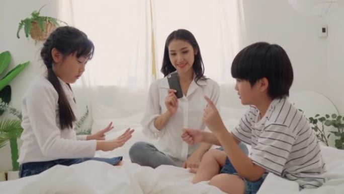 快乐的亚洲家庭在房间的床上玩石头剪刀游戏