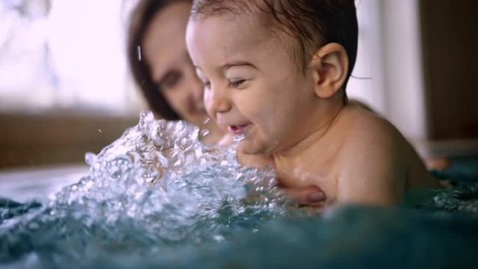 快乐的宝宝在室内游泳池里泼水和妈妈玩耍