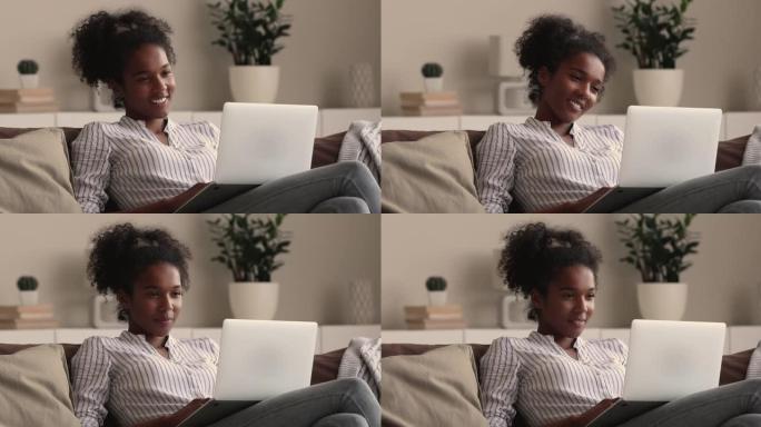 轻松的千禧一代微笑的非洲混血妇女使用笔记本电脑。