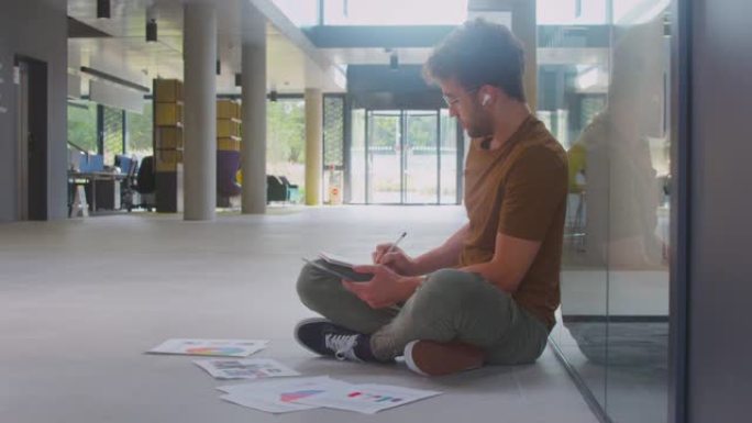 使用数字平板电脑坐在大学大楼地板上的男大学生