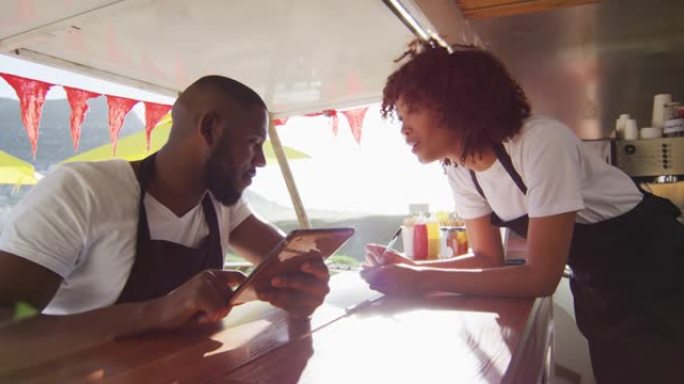 非裔美国夫妇穿着使用数字平板电脑的围裙，并在餐车上做笔记