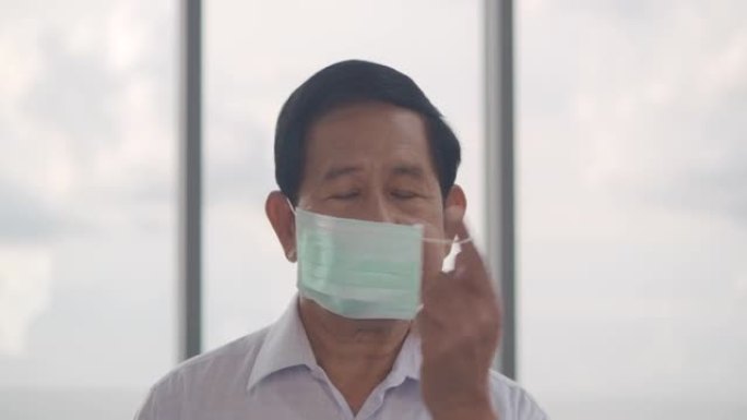 肖像62岁的亚洲老年男子摘下医用面具，微笑着看着镜头。口罩及面罩(非白种人)