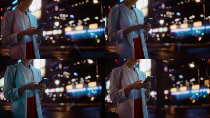 匿名女性使用智能手机走过充满霓虹灯的夜晚城市街道。女人拿着手机，发布社交媒体，在线购物，发短信。跟踪