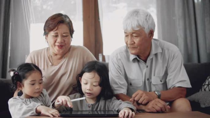 孙儿在数码平板电脑上做家庭作业，与资深成人在家。