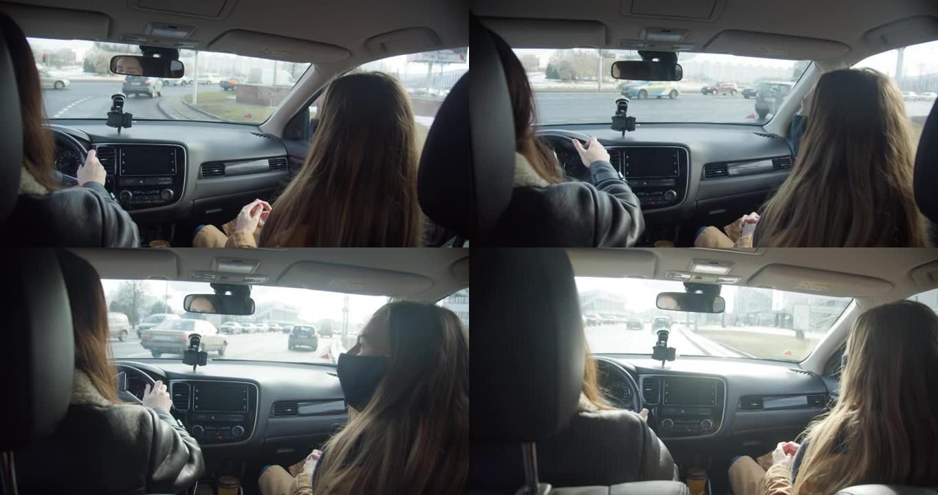 从车内看，两名戴着口罩的女商人在开车时交谈，沿着繁忙的城市街道右转。