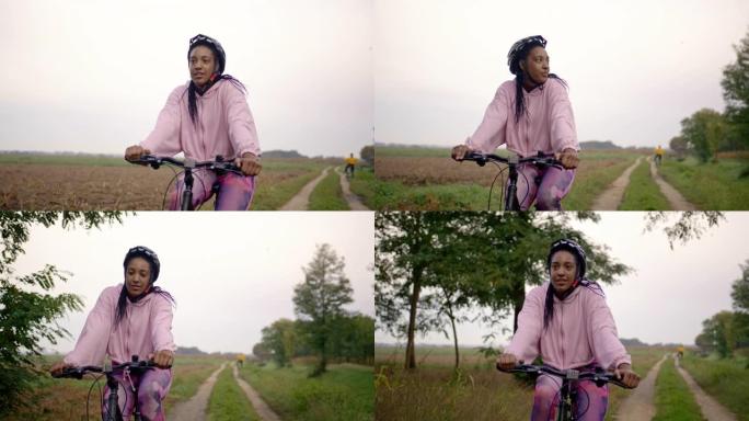 追踪两名成年女性在草地土路上骑自行车的手持照片，与她的伴侣在远处，慢动作镜头