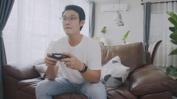 宽镜头前视图4k分辨率有吸引力的亚洲成年人拿着操纵杆或游戏控制器，在家玩视频游戏机。人的反应享受他在