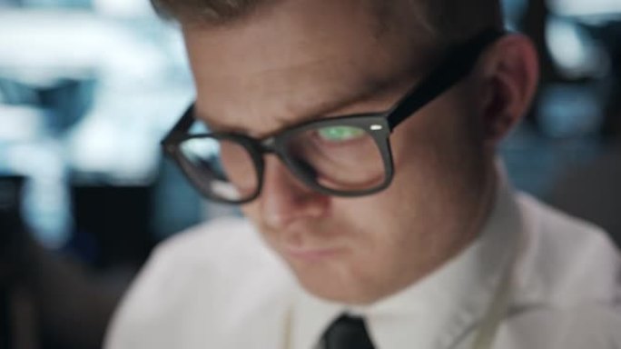 一名戴眼镜的男子正专注地在电脑前工作，这是他脸部的特写。