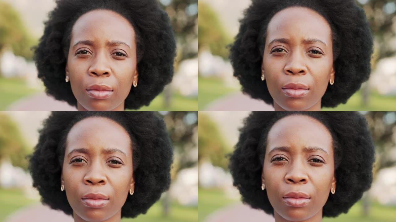 脸，头和头发，一个黑人妇女独自站在外面，表情茫然地看着镜头。绿色背景下一位严肃的年轻非洲裔美国女性户