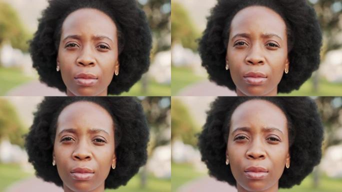 脸，头和头发，一个黑人妇女独自站在外面，表情茫然地看着镜头。绿色背景下一位严肃的年轻非洲裔美国女性户