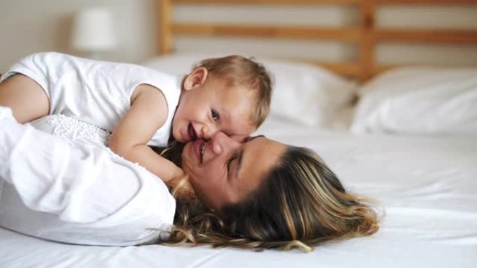 一位年轻快乐微笑的neo母亲的真实照片很喜欢在卧室里和她刚出生的婴儿玩得开心