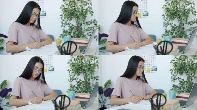 年轻的亚洲女士看着笔记本电脑屏幕，在公寓里写家庭作业