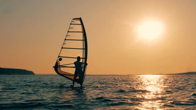 一名男子在日落时在海里冲浪风帆