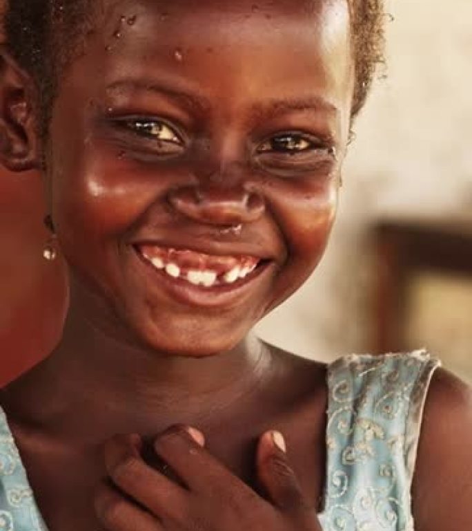 一个害羞的真实的非洲女孩的特写肖像，对着模糊背景的相机微笑。对未来充满希望的黑人女性与世界团结