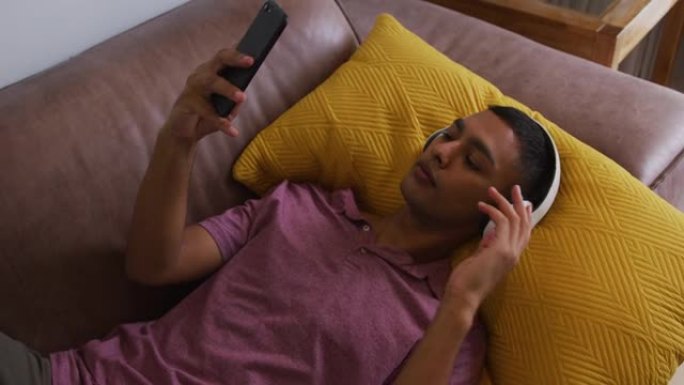 混血男子戴着耳机躺在沙发上使用智能手机