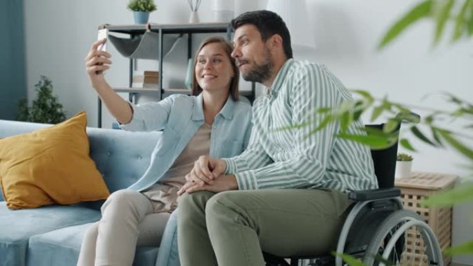 坐在轮椅上的快乐夫妇和在家用智能手机相机自拍的女人