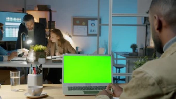 非裔美国上班族晚上在工作场所使用带色度键绿屏的笔记本电脑