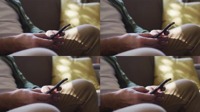 坐在沙发上的白人男子的手的特写镜头，在家中使用智能手机