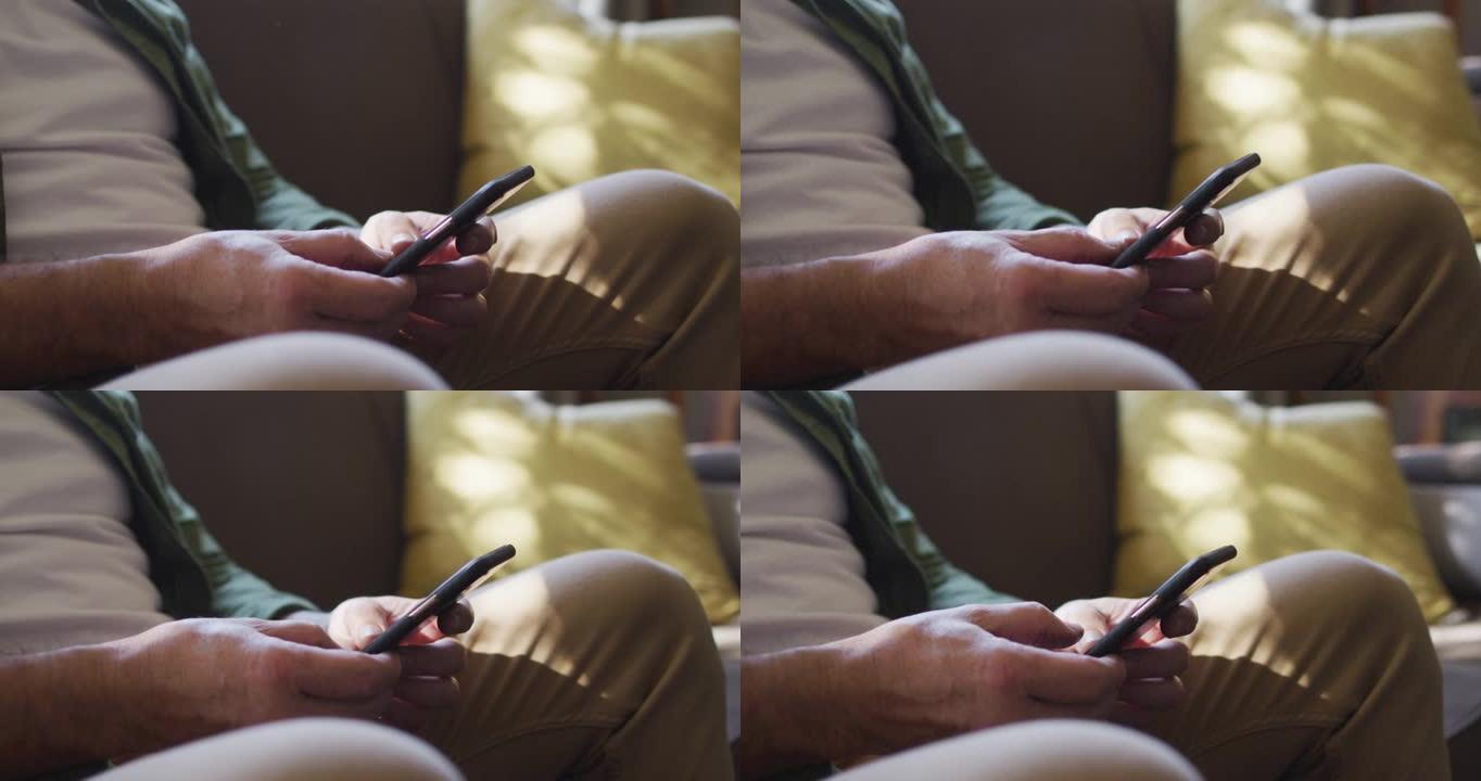 坐在沙发上的白人男子的手的特写镜头，在家中使用智能手机