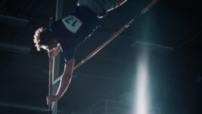 撑竿跳高跳高冠军: 职业男运动员用杆子跑成功跳过杠铃，脚上着地。戏剧性的色彩，运动成就的慢动作特写镜