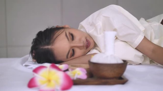 年轻的亚洲妇女躺在床上放松，在水疗沙龙里做热石按摩