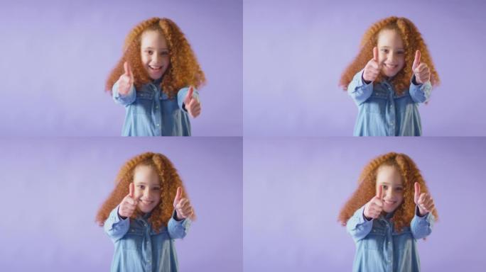 工作室拍摄的红头发微笑的女孩在紫色背景下竖起双拇指。-慢动作拍摄