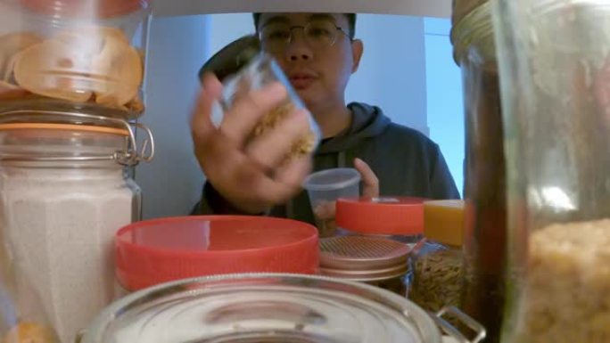 亚洲中国男性从厨房的货架柜里取回食品瓶