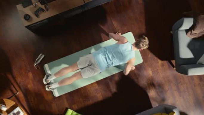 顶视图运动: 男人在家里的垫子上做俯卧撑运动。肌肉发达，身体健康，非常强壮的运动员在他的公寓里锻炼。