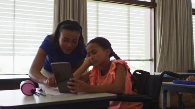 多元化的微笑女教师帮助坐在轮椅上的女学生使用平板电脑