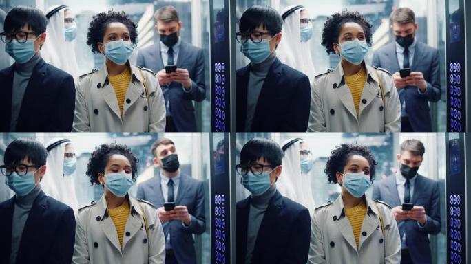 四个戴着防护口罩的多种族国际人士乘坐玻璃电梯前往现代化商务中心的办公室。医疗保健、新型冠状病毒肺炎大