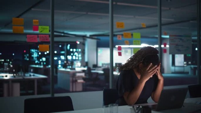 深夜在大城市办公室工作的非裔美国女商人在笔记本电脑上工作。疲惫的女性企业家试图找到解决商业问题的方法