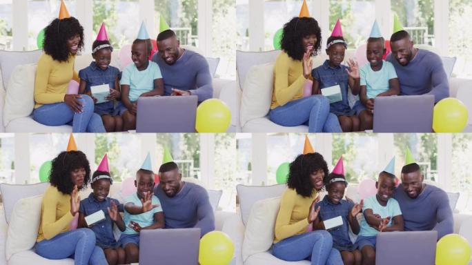 戴着派对帽子的非裔美国人家庭坐在沙发上挥舞着笔记本电脑上的录像带