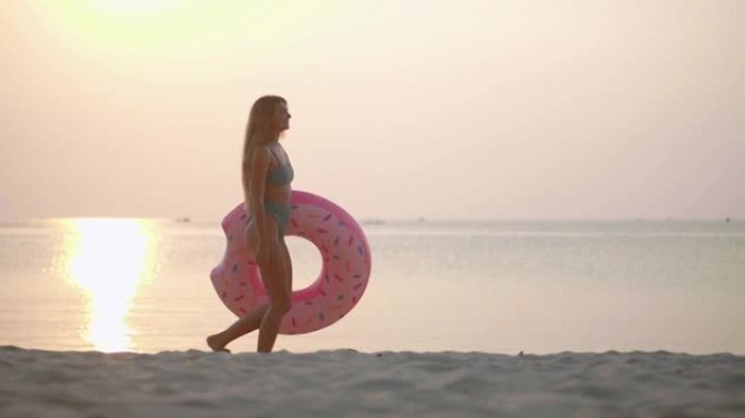 幸福的肖像27岁的拉丁美洲和西班牙裔年轻女子穿着绿色比基尼，在热带海滩上戴着粉红色的橡胶圈，沿着日落