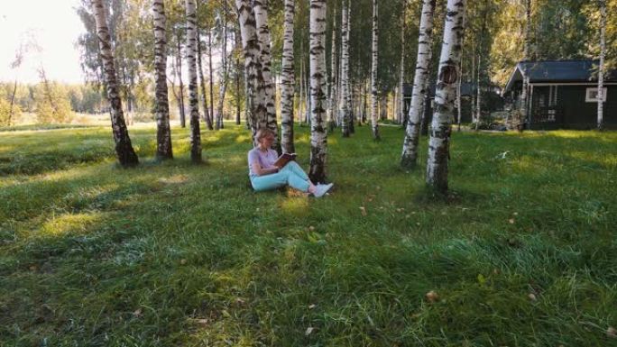 女人坐在外面的桦树附近看书