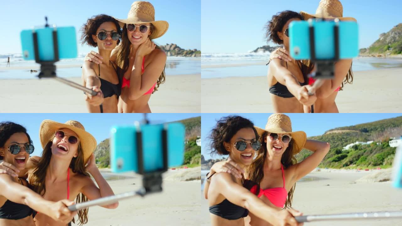 两个有魅力的朋友在海滩上用自拍杆在手机上自拍的4k视频片段