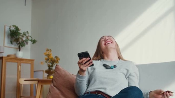 美丽幸福的年轻女子在智能手机购物支付应用程序中输入卡号，在light home愉快地向后倾斜。