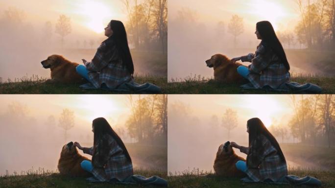 年轻女子坐在雾湖附近时使用手机和抚摸狗