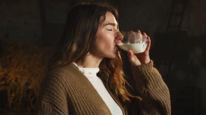 电影特写镜头，年轻的女农民喝新鲜的刚生产的生物牛奶，用于真正的乳制品行业，并在农村奶牛场的牛棚马st