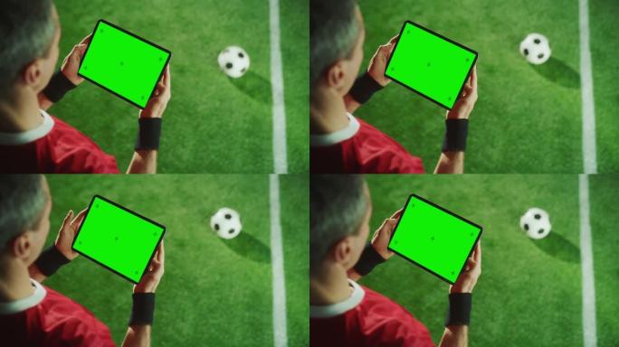 职业足球运动员手持数字平板电脑与绿色屏幕色度键与运动标记。从上到下拍摄的足球明星浏览内容，而站在赛场