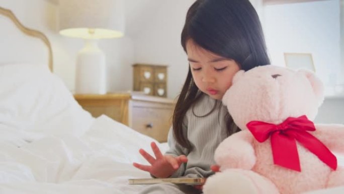 年轻女孩坐在床上，手机穿着睡衣在家拥抱泰迪熊-慢动作拍摄