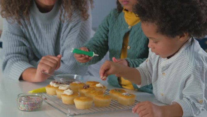 母亲和孩子在厨房一起装饰纸杯蛋糕的特写