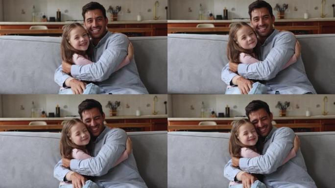小美丽的女儿拥抱年轻的继父坐在舒适的沙发上