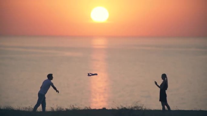 男人和女人把玩具飞机扔在日落背景上