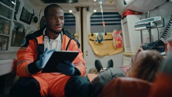 黑人非裔美国EMS专业护理人员使用平板电脑为受伤患者在去医院的途中填写问卷。紧急医疗助理在救护车上工