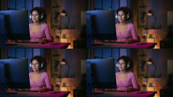 年轻迷人的黑人女性晚上在时尚的阁楼公寓里使用台式电脑。富有创造力的女性微笑，查看社交媒体，浏览互联网