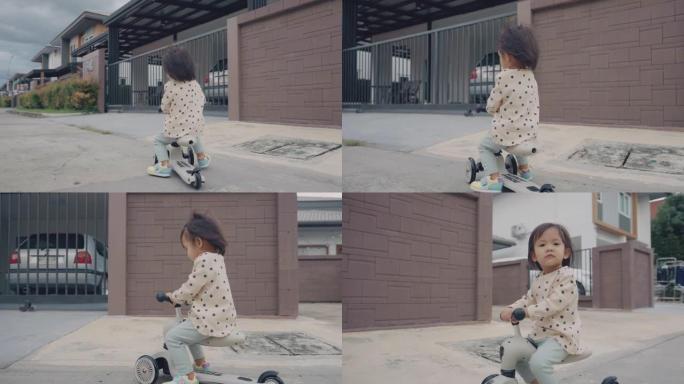 一个小女孩骑着一辆没有头盔的蹒跚学步的踏板车，微笑着。