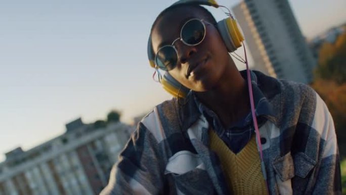 年轻时尚的黑人妇女，戴着黄色耳机，在日落时在城市背景上听音乐和跳舞。充满活力的自信年轻女性跟随节拍并