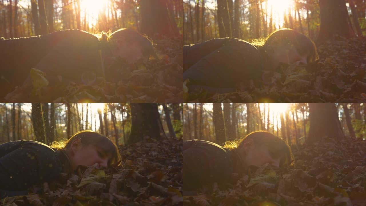 特写: 年轻女子在秋天的森林里慢跑时掉进了一堆树叶里。